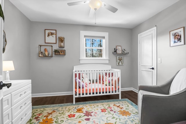 bedroom featuring a nursery area, ceiling fan, wood finished floors, and baseboards