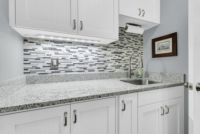 kitchen featuring light stone counters, white cabinets, tasteful backsplash, and sink