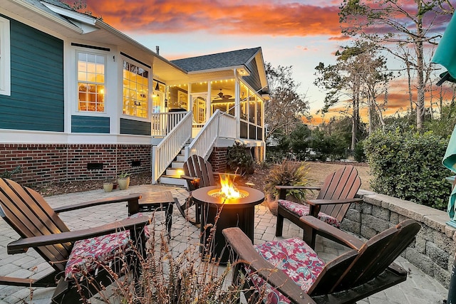 patio terrace at dusk with ceiling fan, an outdoor fire pit, and a sunroom