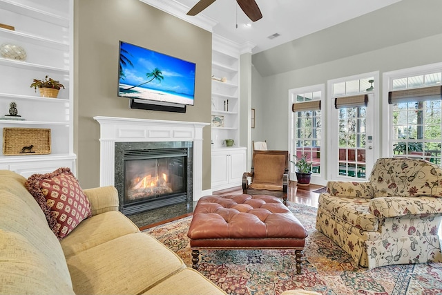 living room featuring ceiling fan, wood-type flooring, a premium fireplace, built in shelves, and crown molding