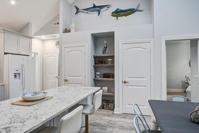 16 Oakwood Ln, Edisto Island, SC 29438 - kitchen with white refrigerator with ice dispenser, a breakfast bar area, light wood-style flooring, light stone countertops, and high vaulted ceiling