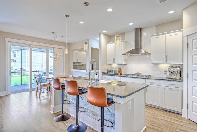 2336 Brinkley Rd, Johns Island, SC 29455 - kitchen with wall chimney exhaust hood, stainless steel gas stovetop, a kitchen island with sink, light wood finished floors, and backsplash