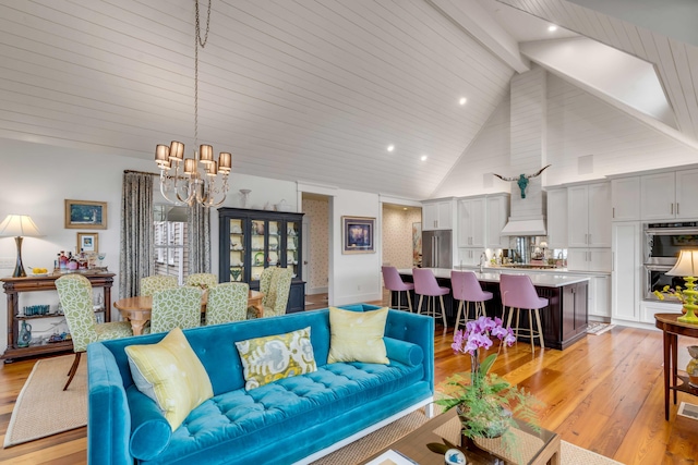 living room featuring beam ceiling, high vaulted ceiling, a chandelier, and light wood-type flooring