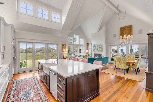 kitchen featuring sink, dark brown cabinets, light hardwood / wood-style floors, a center island with sink, and french doors