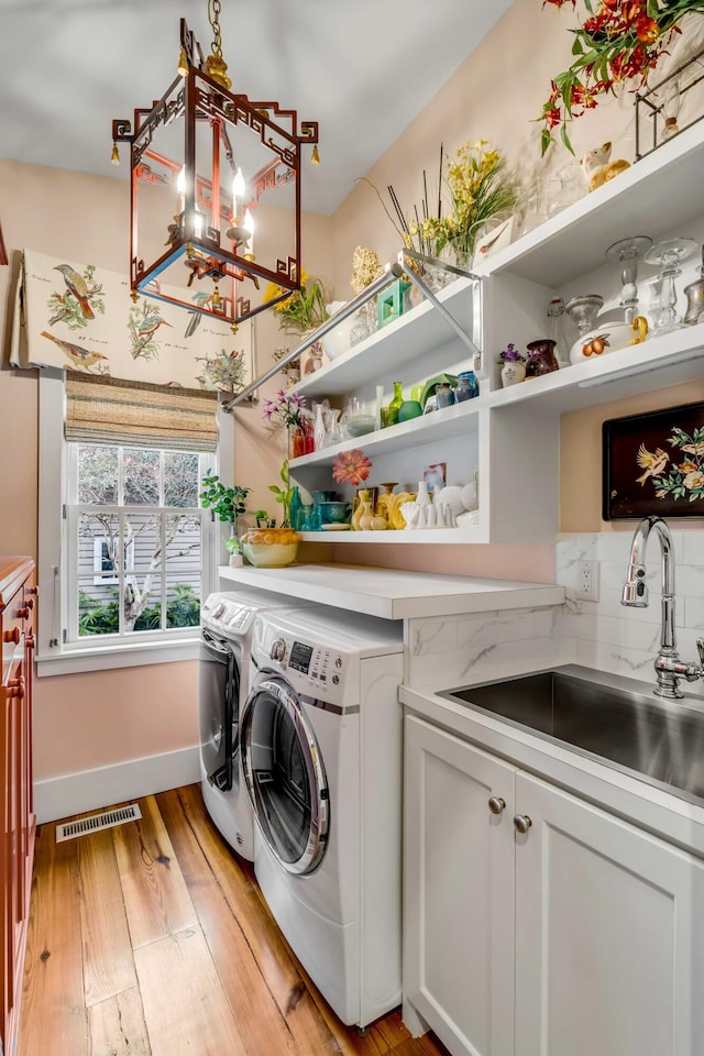 laundry room featuring cabinets, washer and clothes dryer, sink, and light hardwood / wood-style flooring