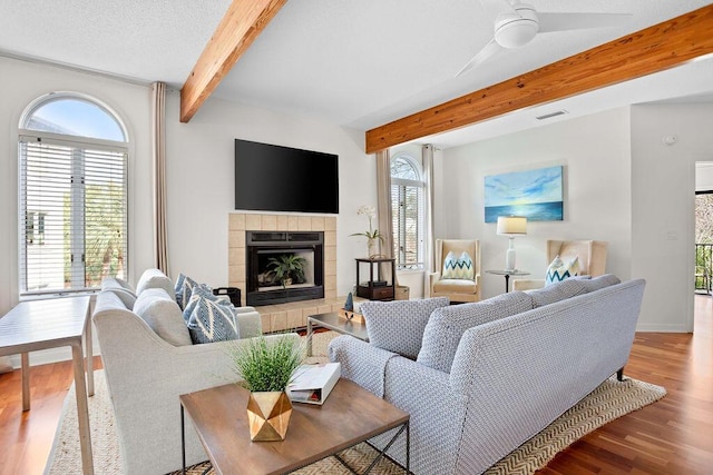 living room with a fireplace, wood-type flooring, ceiling fan, and beamed ceiling