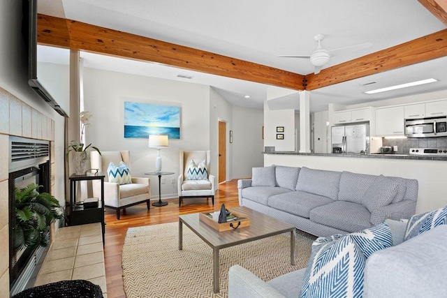 living room featuring beamed ceiling, ceiling fan, and light wood-type flooring