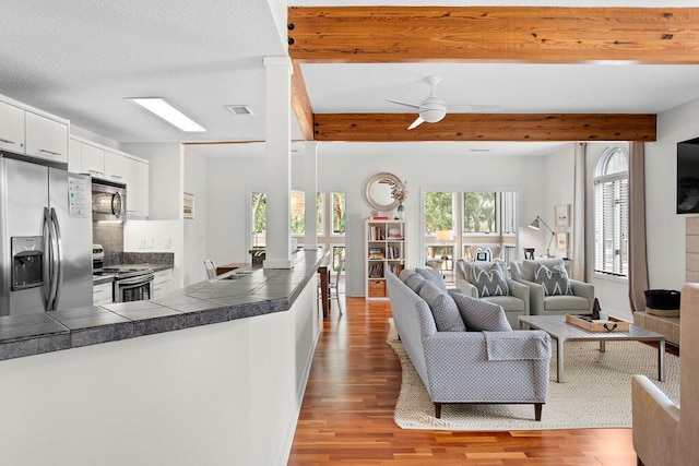 living room with beam ceiling, ceiling fan, light hardwood / wood-style flooring, and sink