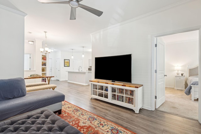 living room featuring ornamental molding, hardwood / wood-style floors, sink, and ceiling fan with notable chandelier