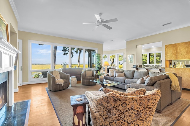 living room with light hardwood / wood-style flooring, crown molding, a high end fireplace, and ceiling fan