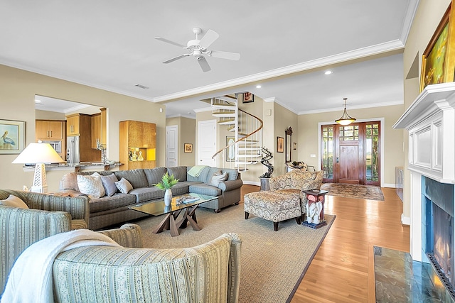 living room featuring ceiling fan, ornamental molding, a fireplace, and light hardwood / wood-style flooring