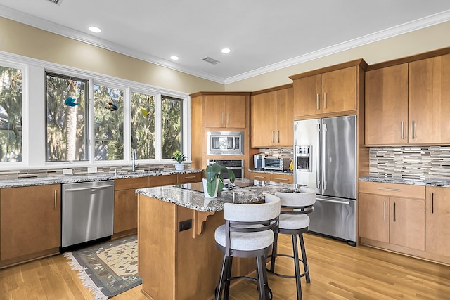 kitchen featuring a kitchen island, appliances with stainless steel finishes, ornamental molding, light stone countertops, and light wood-type flooring