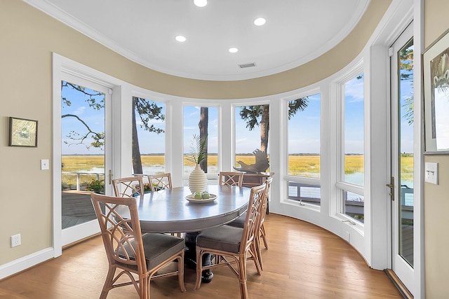 dining space featuring light wood-type flooring, ornamental molding, and a water view