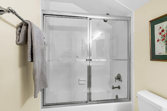 bathroom featuring toilet and combined bath / shower with glass door