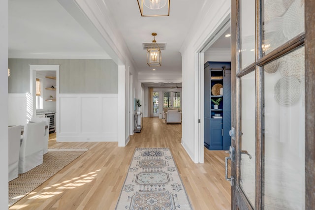 entryway featuring light wood-type flooring, a wainscoted wall, visible vents, and ornamental molding