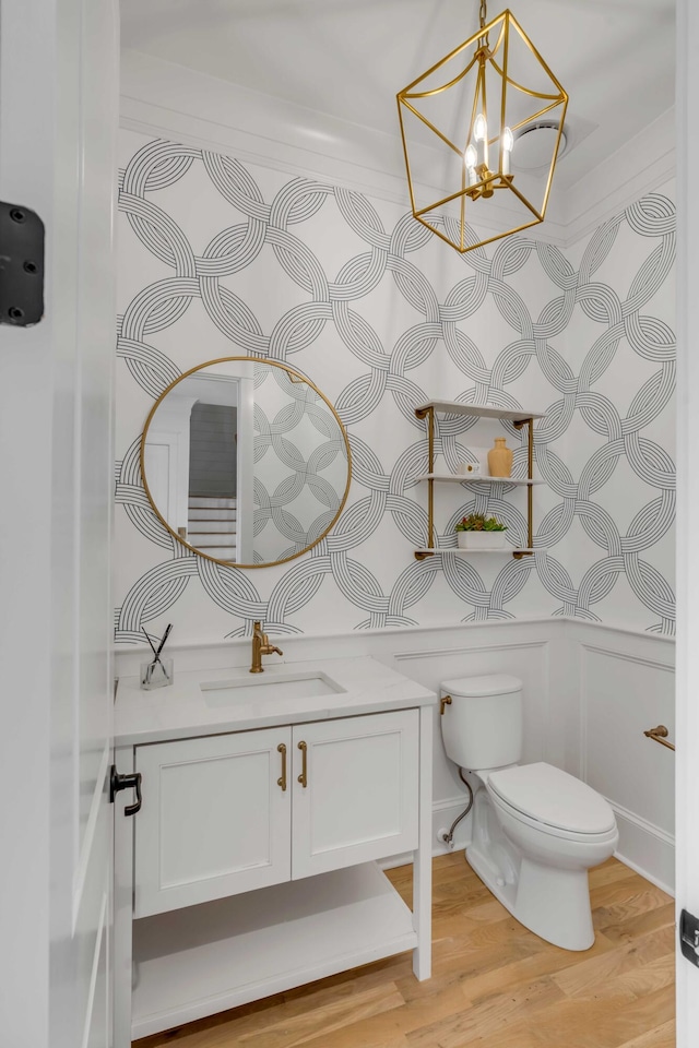 bathroom with a notable chandelier, vanity, toilet, and wood finished floors