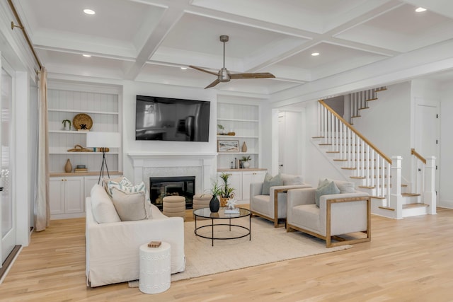 living room with stairway, a glass covered fireplace, coffered ceiling, and light wood-style flooring