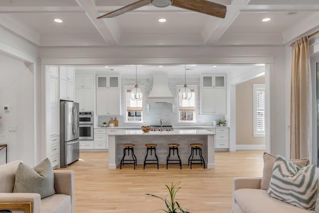 kitchen featuring custom exhaust hood, light countertops, appliances with stainless steel finishes, open floor plan, and a kitchen breakfast bar