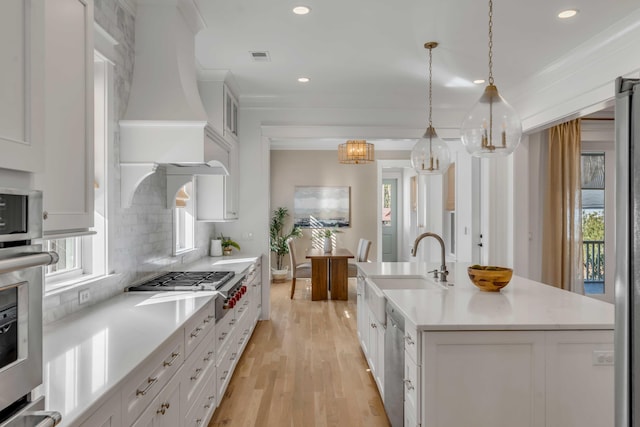 kitchen featuring stainless steel appliances, light countertops, backsplash, a kitchen island with sink, and premium range hood