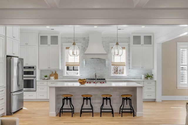 kitchen with custom range hood, appliances with stainless steel finishes, a breakfast bar, and a center island with sink