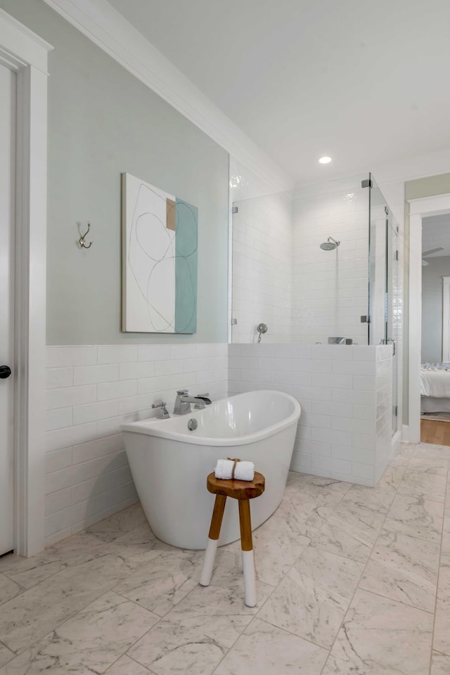 bathroom with a stall shower, a soaking tub, ornamental molding, marble finish floor, and tile walls