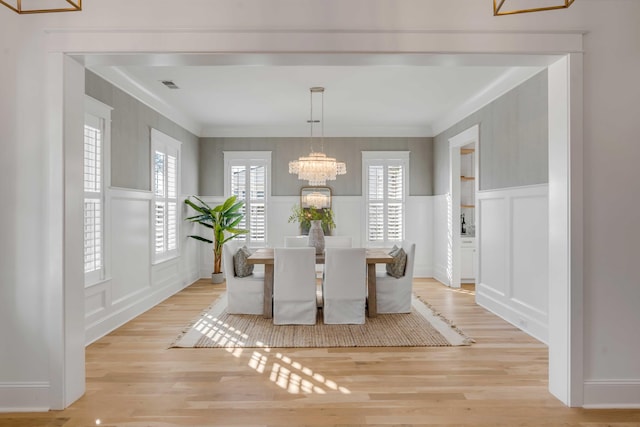 dining space featuring light wood-type flooring, a wainscoted wall, a decorative wall, and crown molding