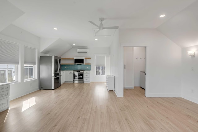 unfurnished living room with lofted ceiling, an AC wall unit, baseboards, and light wood-style floors