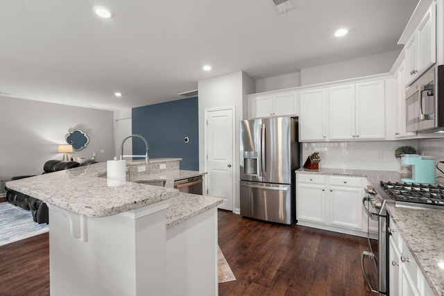 kitchen with a breakfast bar area, stainless steel appliances, light stone countertops, white cabinets, and a center island with sink