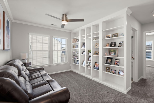 living area featuring ceiling fan, dark carpet, ornamental molding, and a healthy amount of sunlight