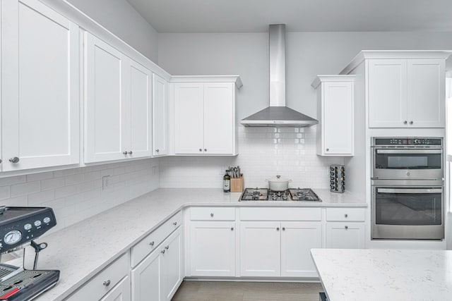 kitchen with white cabinets, backsplash, appliances with stainless steel finishes, and wall chimney exhaust hood