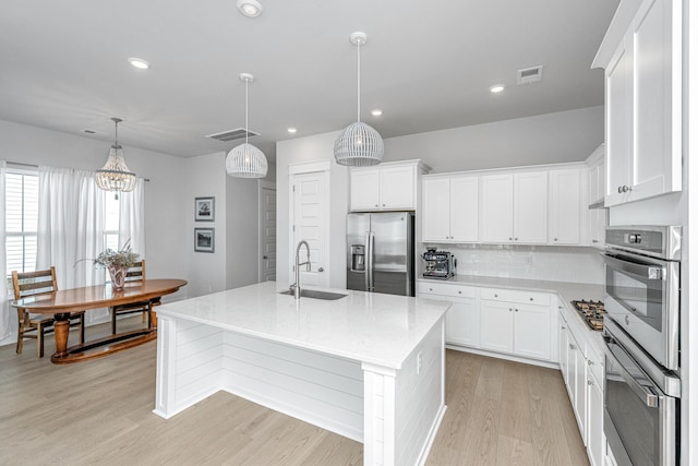 kitchen featuring pendant lighting, sink, white cabinetry, a kitchen island with sink, and appliances with stainless steel finishes