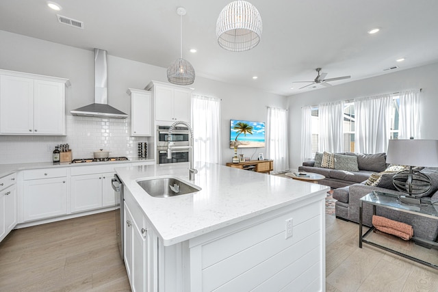 kitchen featuring white cabinetry, sink, stainless steel appliances, and wall chimney range hood