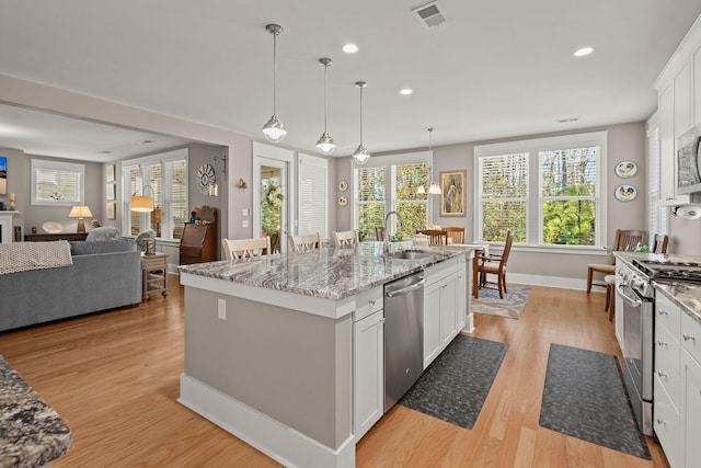 kitchen featuring white cabinets, appliances with stainless steel finishes, sink, a kitchen island with sink, and light stone counters