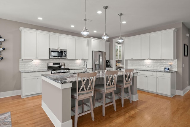 kitchen featuring white cabinets, appliances with stainless steel finishes, a center island with sink, and dark stone counters