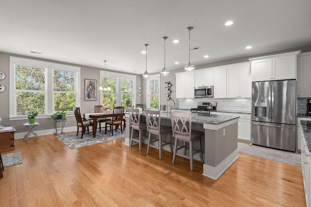 kitchen featuring white cabinetry, decorative light fixtures, stainless steel appliances, light stone counters, and a center island with sink