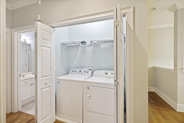 clothes washing area featuring sink, crown molding, independent washer and dryer, and light wood-type flooring