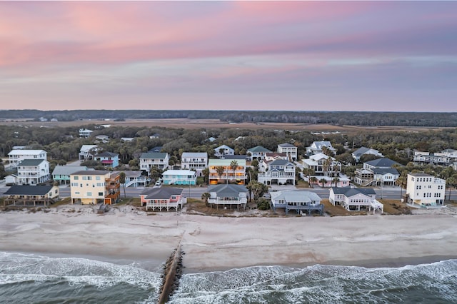 aerial view at dusk featuring a water view and a beach view