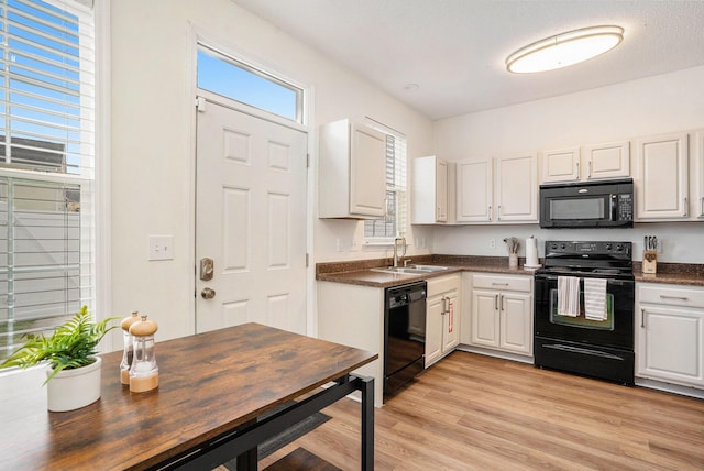 kitchen with a sink, white cabinetry, light wood-style floors, black appliances, and dark countertops