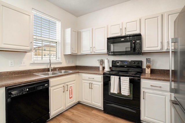 kitchen featuring dark countertops, black appliances, white cabinets, and a sink