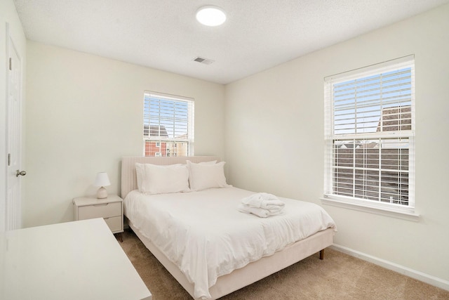 carpeted bedroom featuring a textured ceiling, visible vents, and baseboards