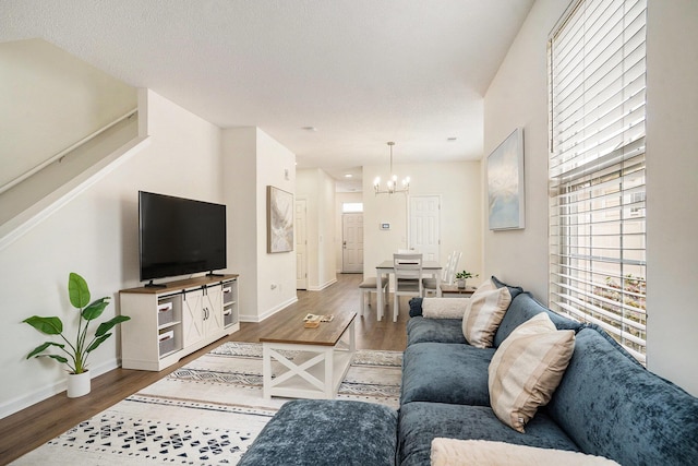 living room featuring a notable chandelier, stairway, a textured ceiling, wood finished floors, and baseboards