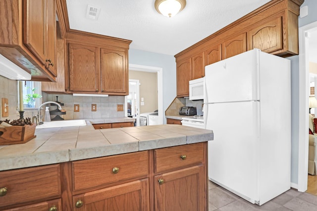 kitchen featuring tile countertops, white appliances, sink, tasteful backsplash, and washing machine and clothes dryer