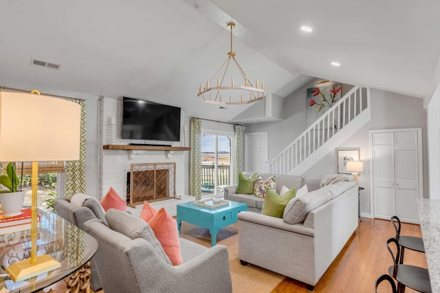 living area with visible vents, stairway, wood finished floors, vaulted ceiling, and a brick fireplace