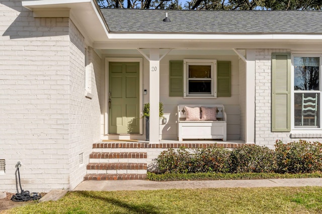 entrance to property with brick siding, a porch, and a shingled roof