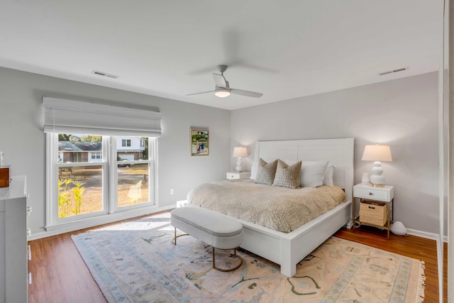 bedroom with a ceiling fan, wood finished floors, visible vents, and baseboards