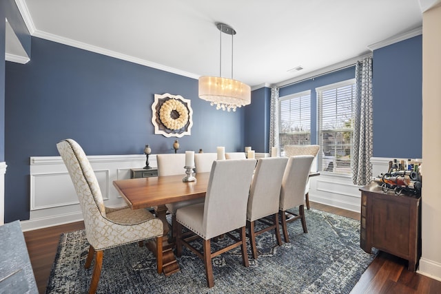 dining area with a wainscoted wall, wood finished floors, crown molding, a decorative wall, and a notable chandelier