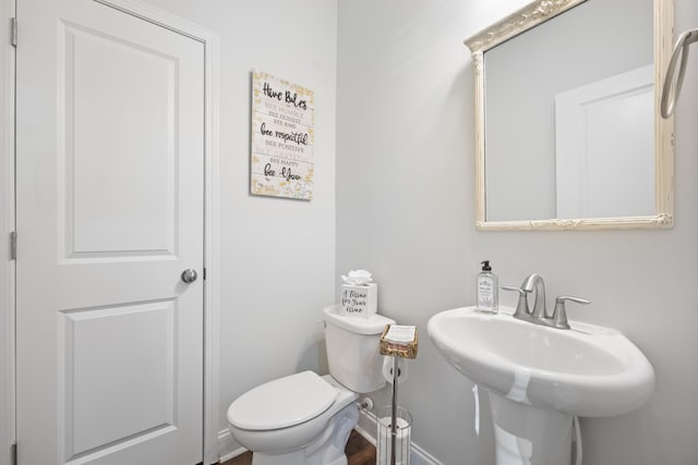 half bathroom featuring toilet, baseboards, and a sink