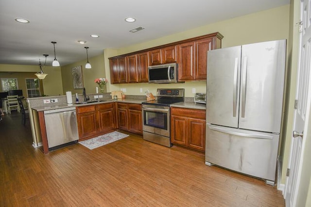 kitchen with hardwood / wood-style flooring, appliances with stainless steel finishes, decorative light fixtures, and sink