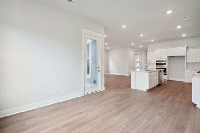 kitchen with a center island with sink, light hardwood / wood-style floors, white cabinetry, stainless steel double oven, and sink