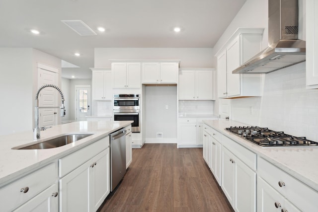 kitchen featuring white cabinets, appliances with stainless steel finishes, wall chimney range hood, and sink